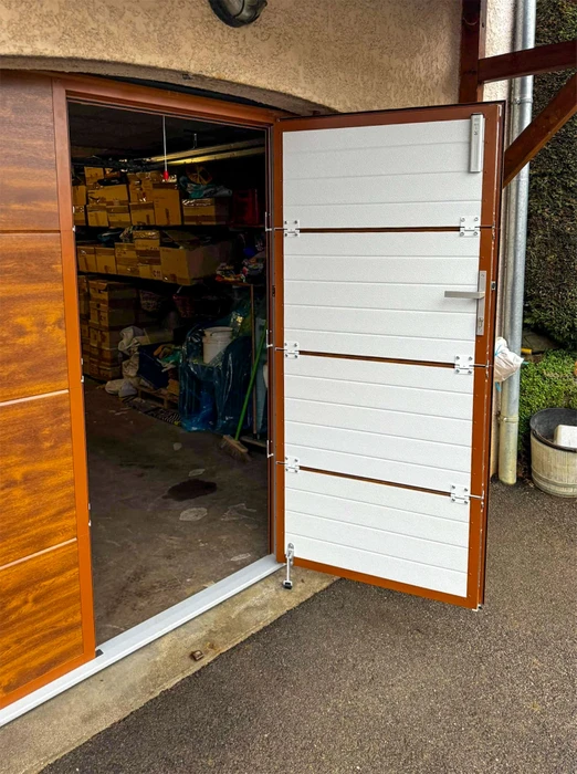 Garage résidentiel avec porte basculante ouverte révélant un espace de stockage encombré de cartons et matériel divers