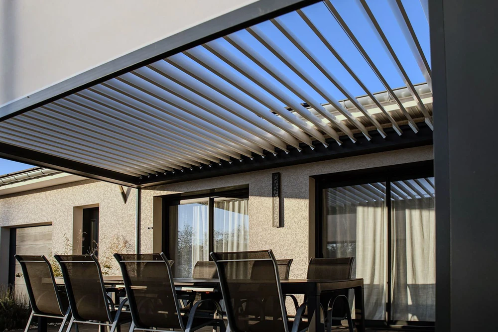 Terrasse couverte moderne en soirée avec pergola en bois, salon de jardin en rotin tressé, chauffe-terrasse au gaz